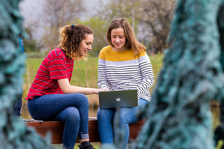 Students looking at laptop sitting at lake
